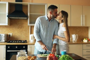 Happy young couple in the kitchen. Handsome man meet and kiss his girlfriend early morning at home